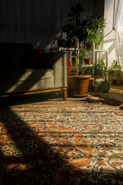 A professional cleaner dressed in a white protective suit, gloves, and blue shoe covers is performing deep carpet cleaning in a bright, minimalist living room. The cleaner is using a vacuum or steam c